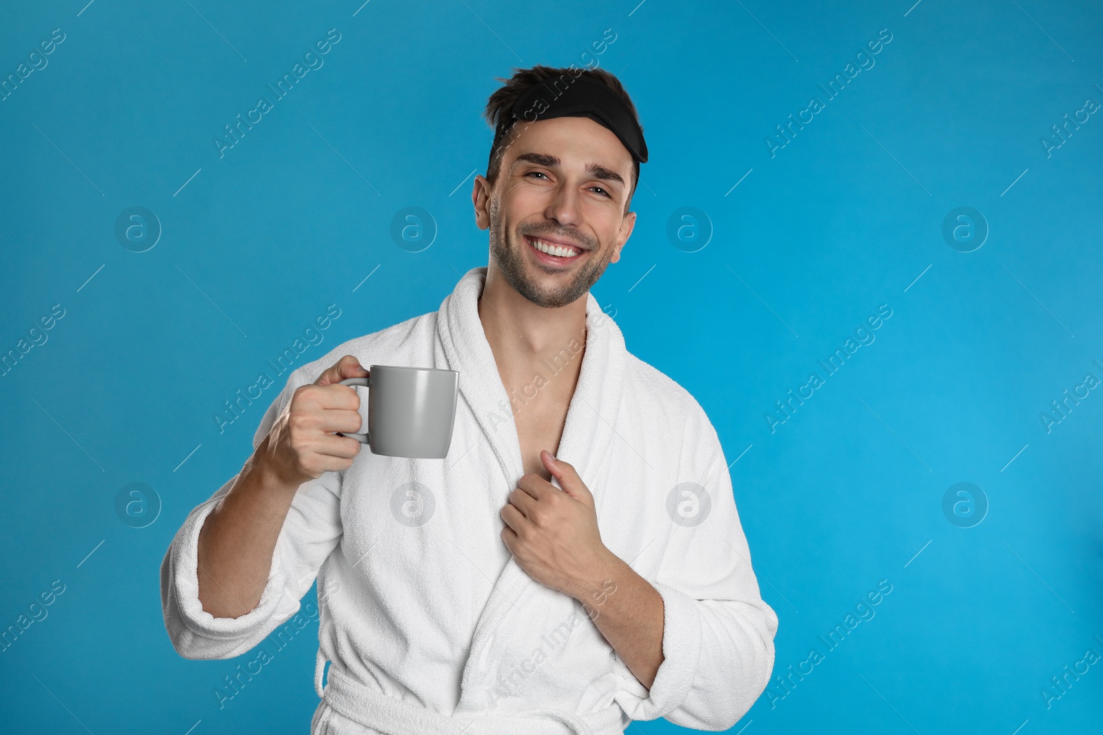 Photo of Young man in bathrobe with cup of coffee on light blue background