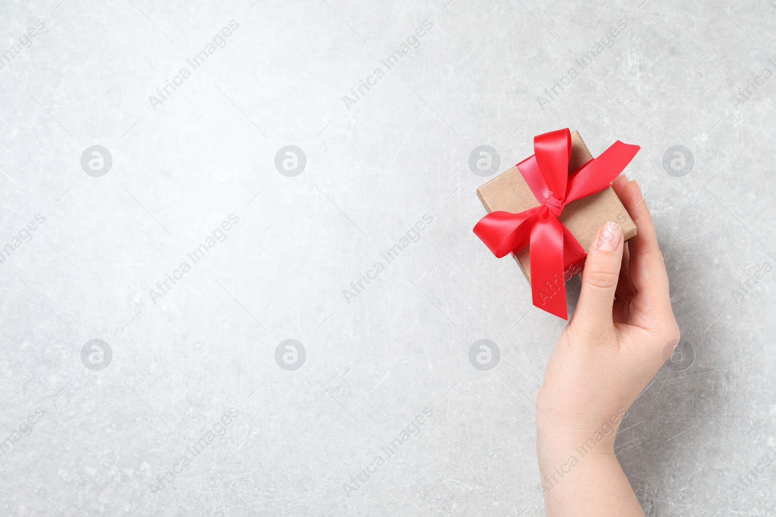 Photo of Woman holding gift box with red bow at light grey table, top view. Space for text