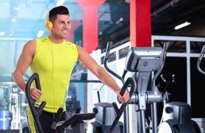 Image of Man using modern elliptical machine in gym, space for text