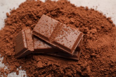Photo of Delicious milk chocolate and cocoa powder on light table, closeup