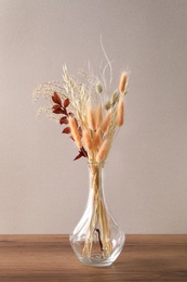 Photo of Dried flowers in vase on wooden table against light background