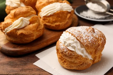 Photo of Delicious profiteroles with cream filling and powdered sugar on wooden table, closeup