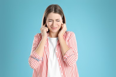 Photo of Emotional young woman covering her ears with fingers on light blue background