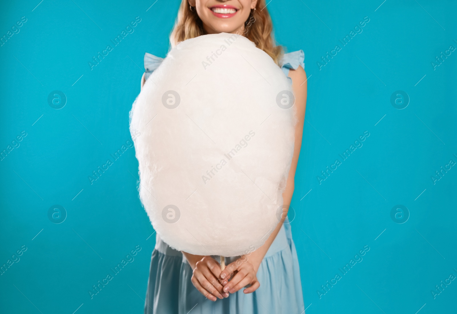 Photo of Young woman with tasty cotton candy on blue background, closeup