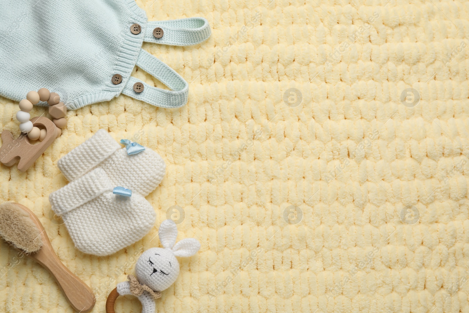 Photo of Cute baby stuff on yellow knitted fabric, flat lay. Space for text