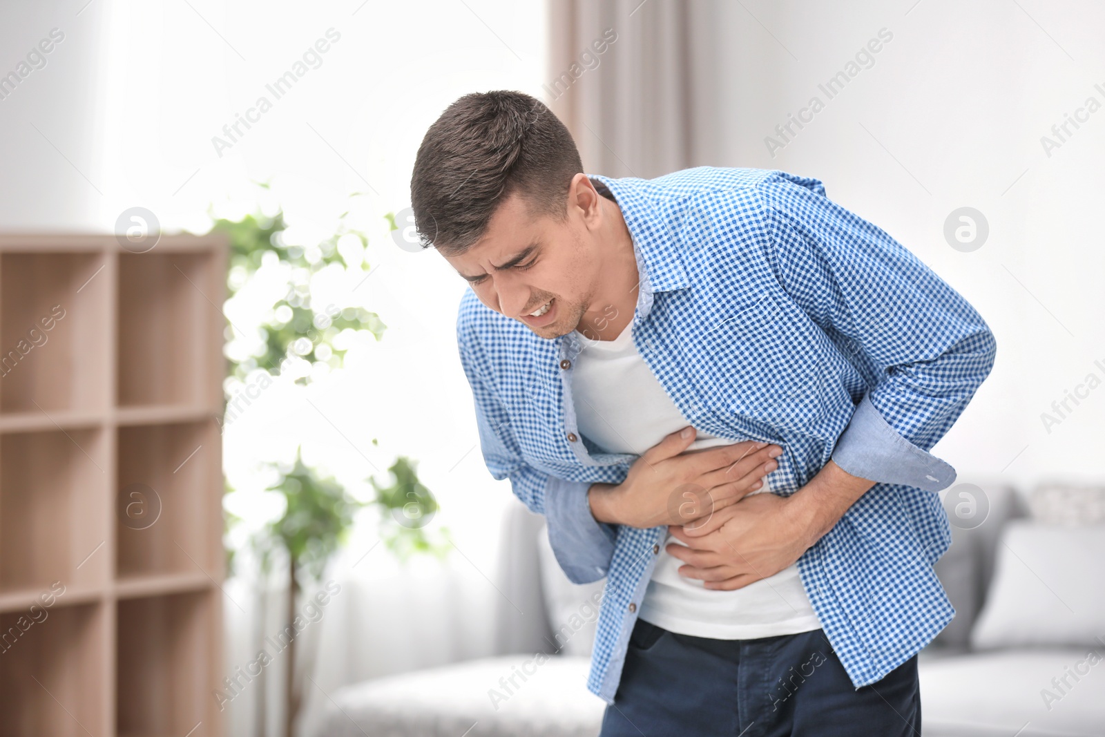 Photo of Young man suffering from stomach ache at home