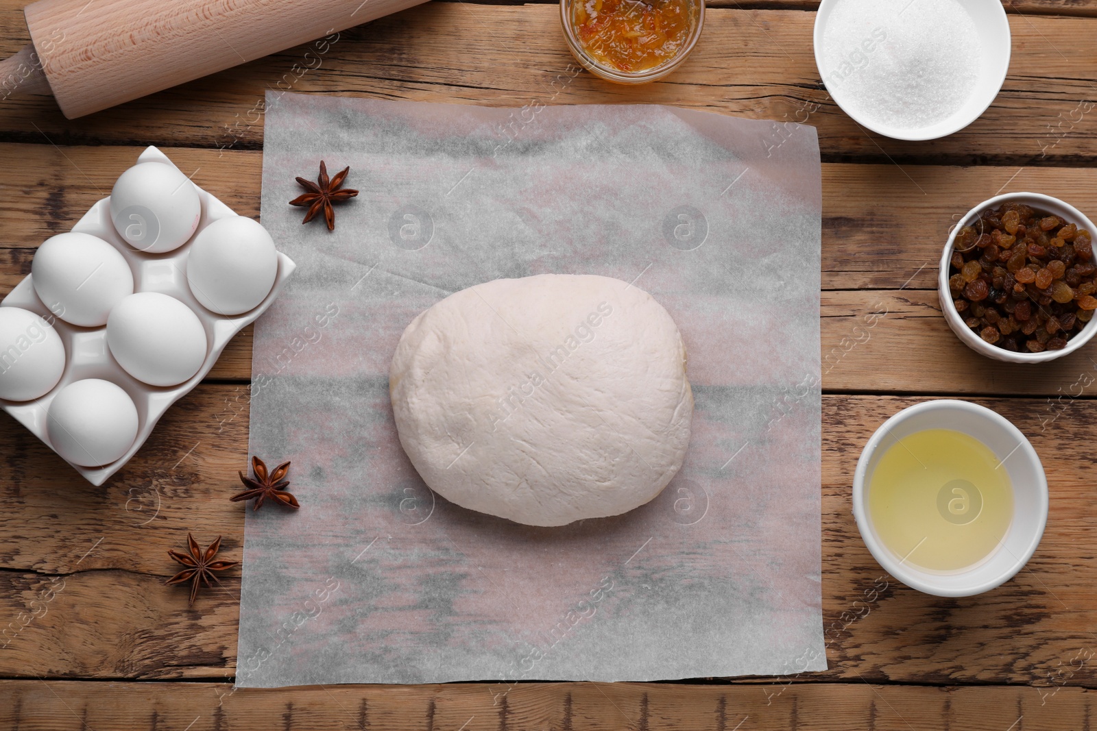 Photo of Baking parchment paper with dough and ingredients on wooden table, flat lay