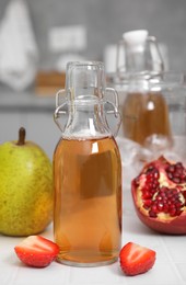 Tasty kombucha in glass bottle and fresh fruits on white tiled table