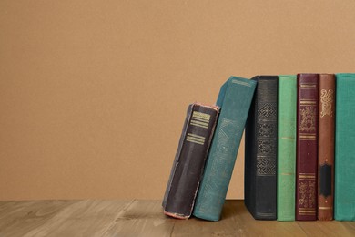 Image of Many hardcover books on wooden table against beige textured background, space for text