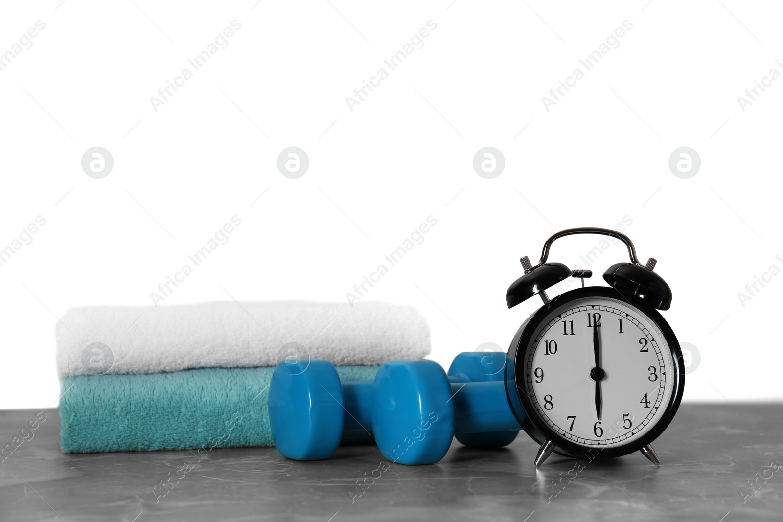 Photo of Alarm clock, towels and dumbbells on marble table against grey background. Morning exercise