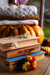 Photo of Stack of books with autumn leaves and flowers as bookmarks on wooden table