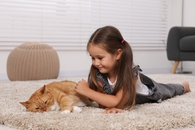 Smiling little girl and cute ginger cat on carpet at home