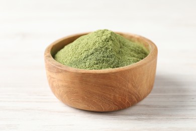 Photo of Wheat grass powder in bowl on white wooden table, closeup