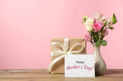 Image of Happy Mother's Day greeting card, gift box and bouquet of beautiful flowers on wooden table