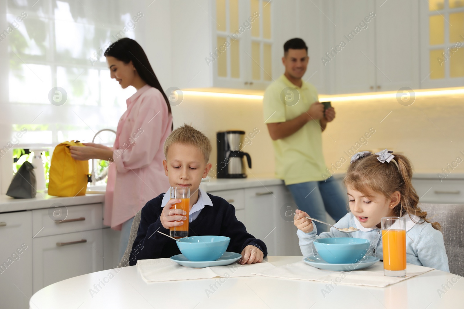 Photo of Kids having breakfast while parents helping them get ready for school in kitchen