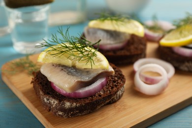 Delicious sandwiches with pieces of salted herring, lemon, onion rings and dill on light blue wooden table, closeup