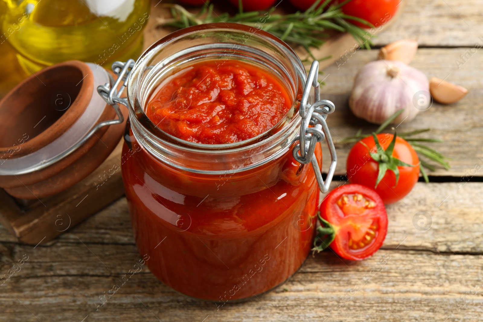 Photo of Homemade tomato sauce in jar and fresh ingredients on wooden table, closeup