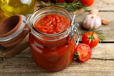 Photo of Homemade tomato sauce in jar and fresh ingredients on wooden table, closeup