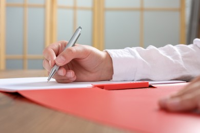 Photo of Woman writing on sheet of paper in red folder at wooden table in office, closeup