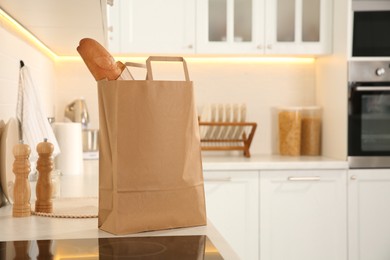 Photo of Paper shopping bag with baguette on white countertop in kitchen. Space for text