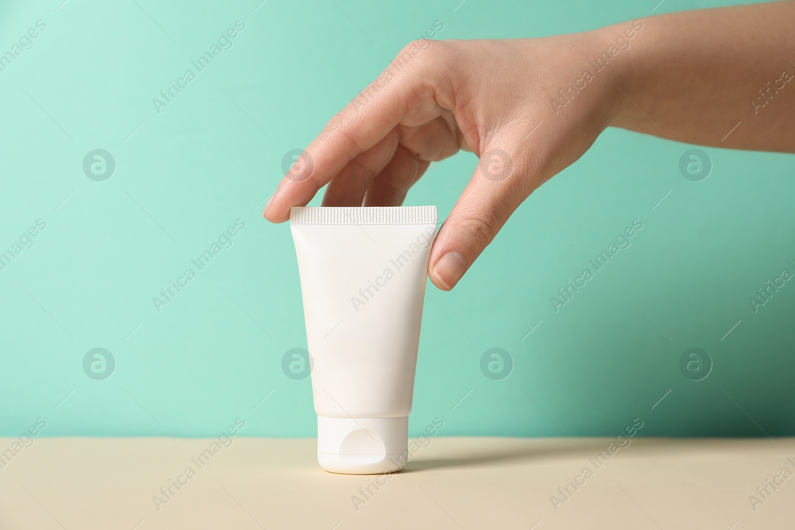 Photo of Tube of hand cream on beige table against turquoise background, closeup