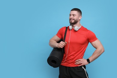 Photo of Handsome man with fitness mat and headphones on light blue background, space for text