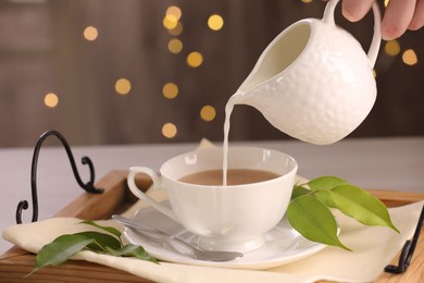 Photo of Woman pouring milk into cup with aromatic tea at table, closeup