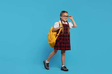 Photo of Happy schoolgirl in glasses with backpack on light blue background