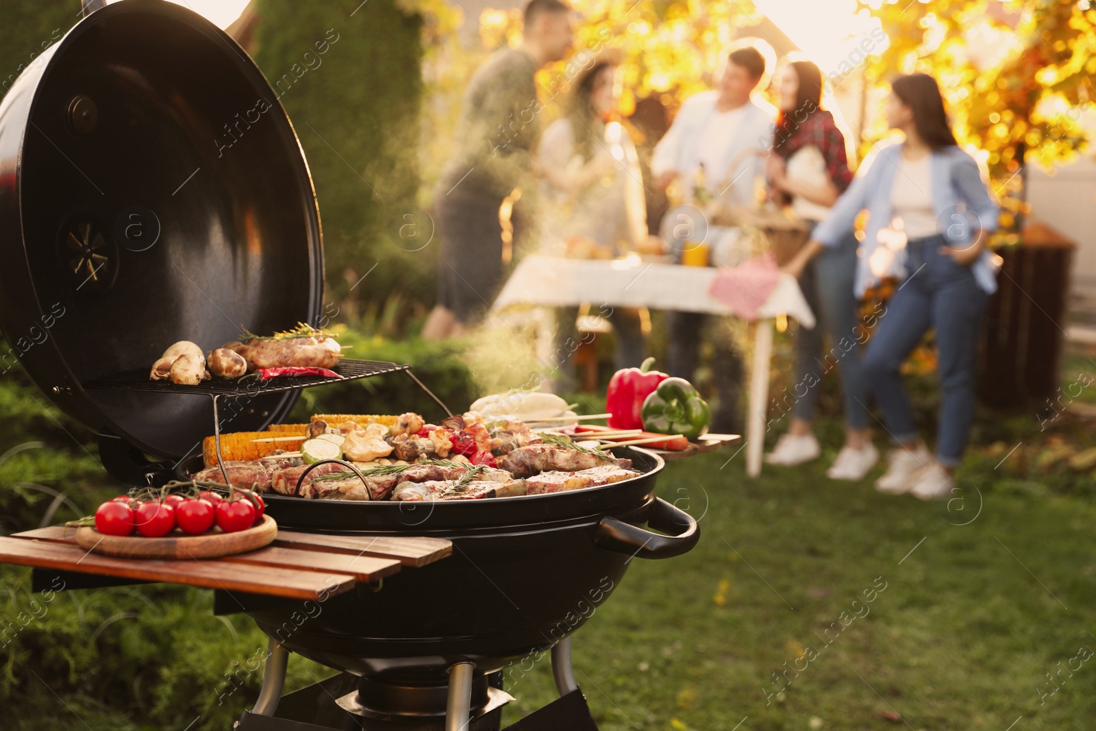 Photo of Group of friends having party outdoors. Focus on barbecue grill with food. Space for text