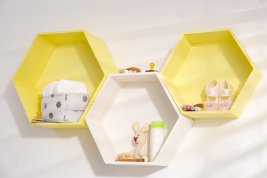 Hexagon shaped shelves with toys and child's accessories on white wall. Interior design