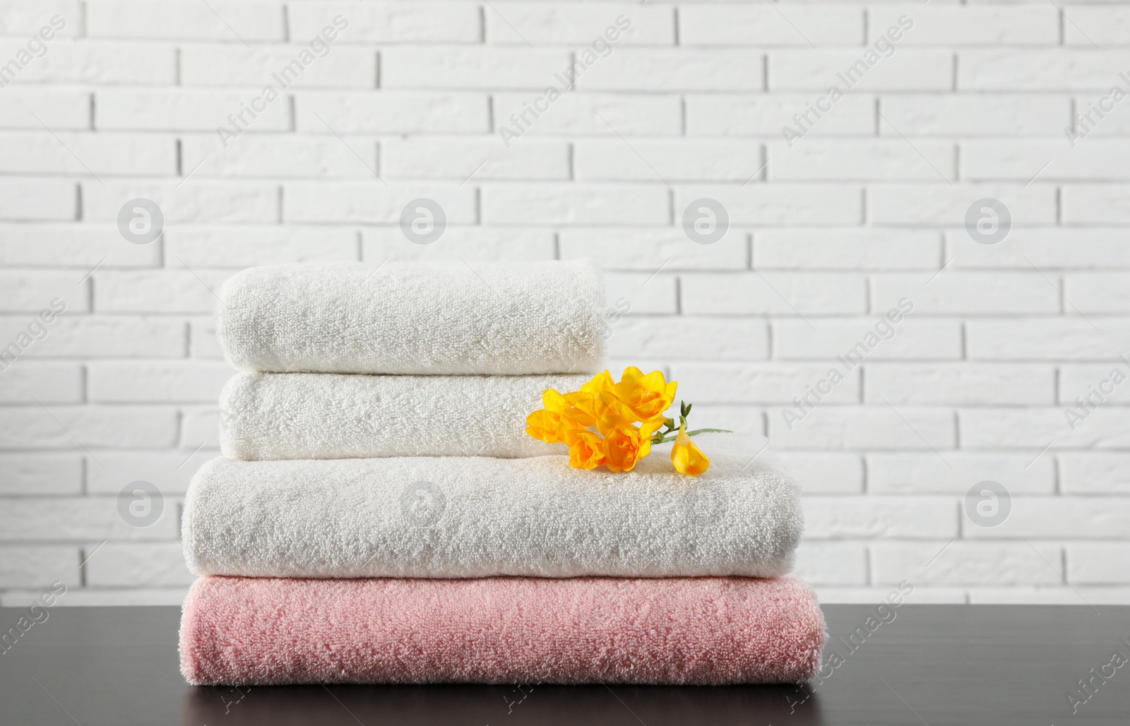 Photo of Stack of folded soft towels with flower on table near brick wall. Space for text