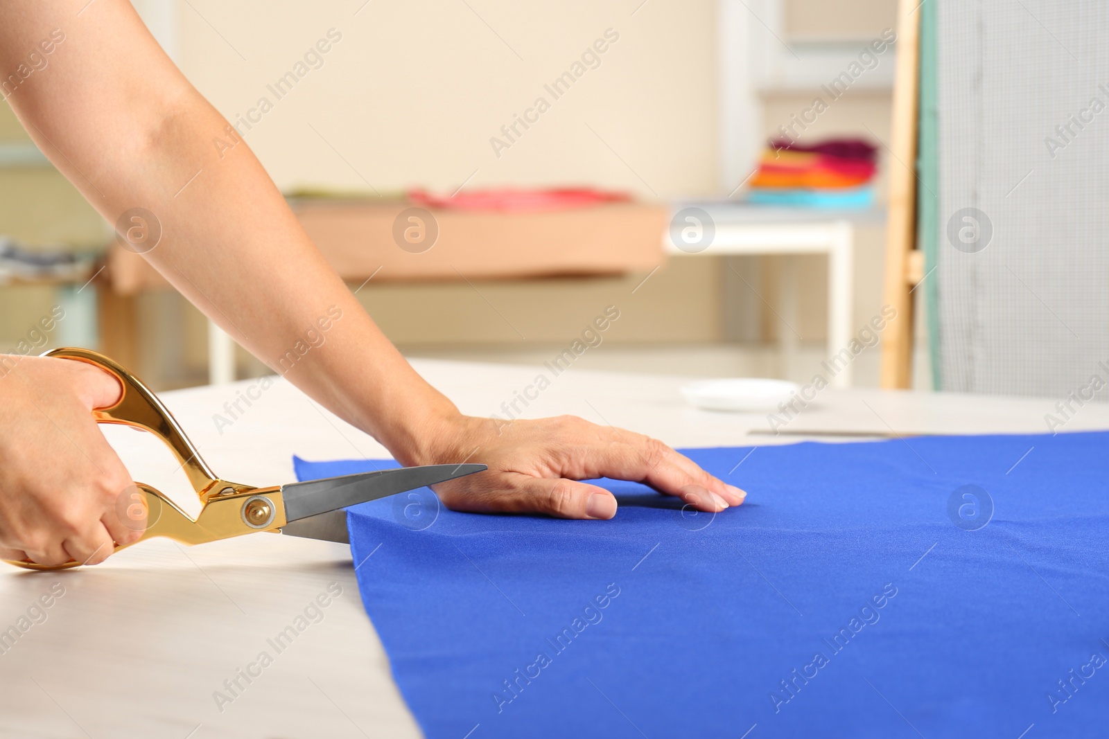 Photo of Seamstress cutting fabric at table in workshop, closeup