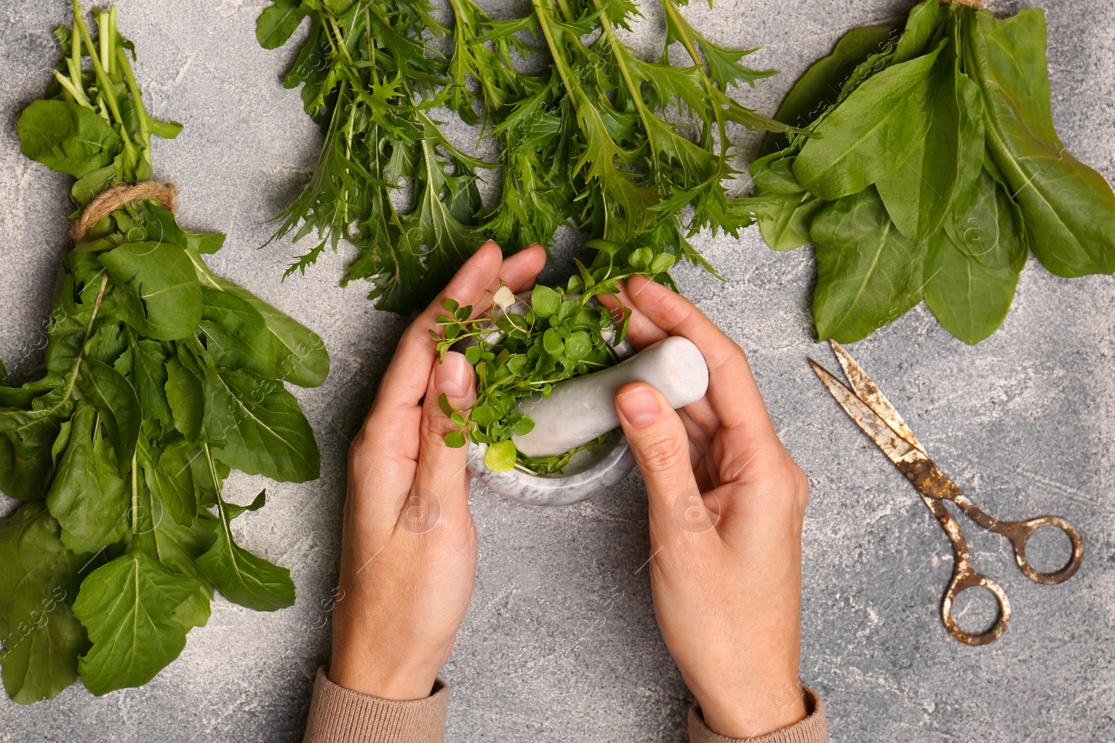 Photo of Woman grinding fresh green herbs in mortar at light grey table, top view