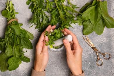 Woman grinding fresh green herbs in mortar at light grey table, top view