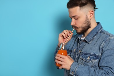 Photo of Handsome young man drinking juice from glass bottle on light blue background. Space for text