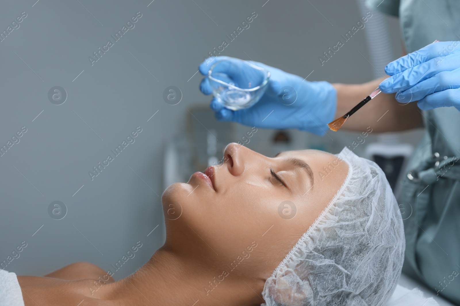 Photo of Cosmetologist applying chemical peel product on client's face in salon