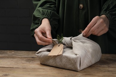Photo of Furoshiki technique. Woman wrapping gift in fabric at wooden table, closeup. Space for text