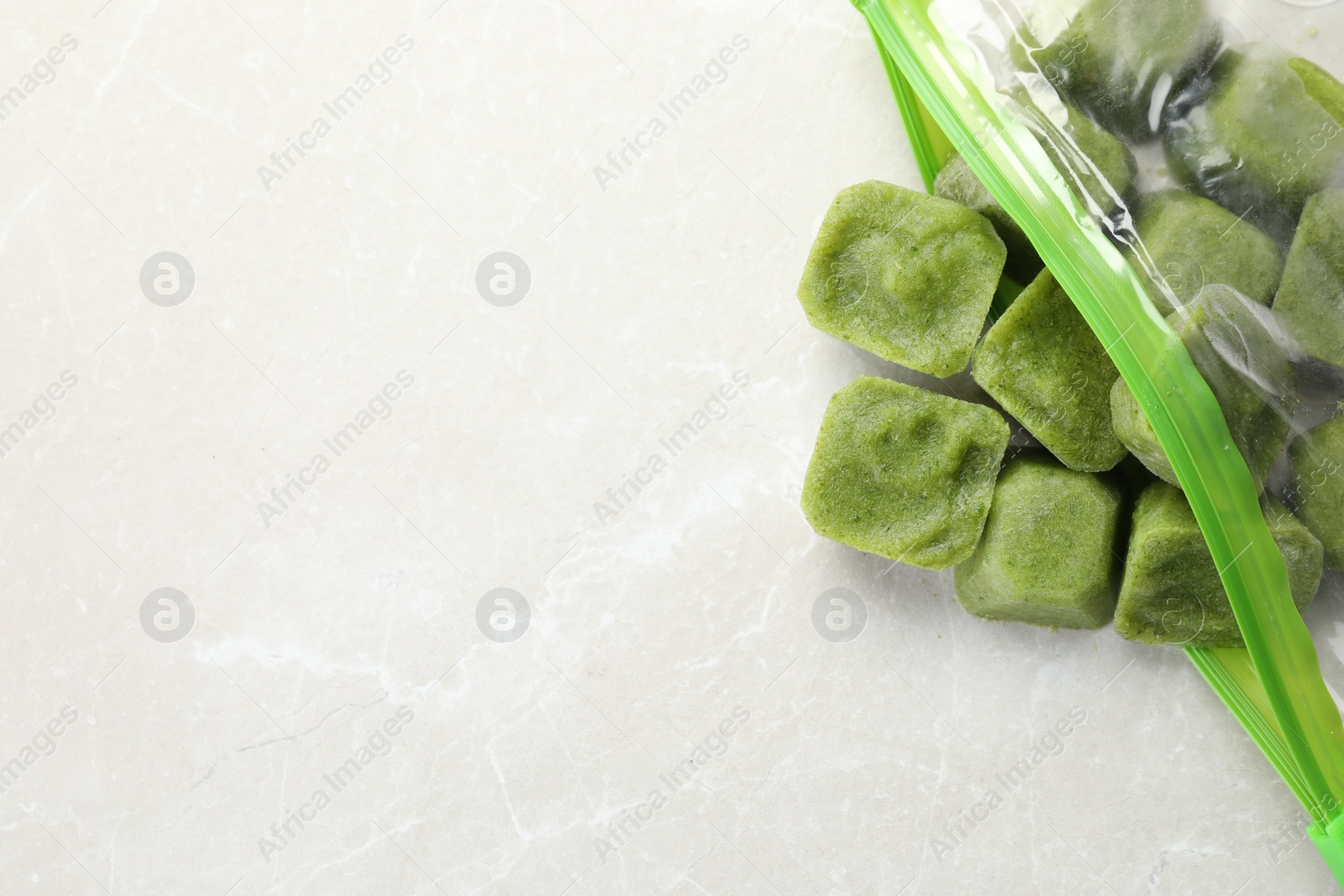 Photo of Frozen broccoli puree cubes in plastic bag on white marble table, top view. Space for text