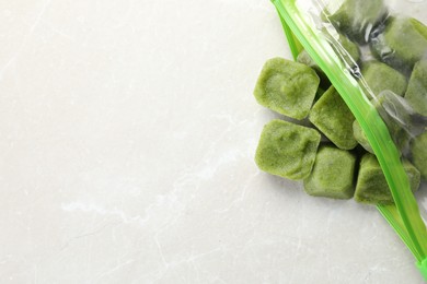 Photo of Frozen broccoli puree cubes in plastic bag on white marble table, top view. Space for text