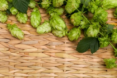 Photo of Fresh green hops and leaves on wicker mat, flat lay. Space for text
