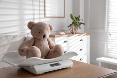 Photo of Baby scales with teddy bear on table in room