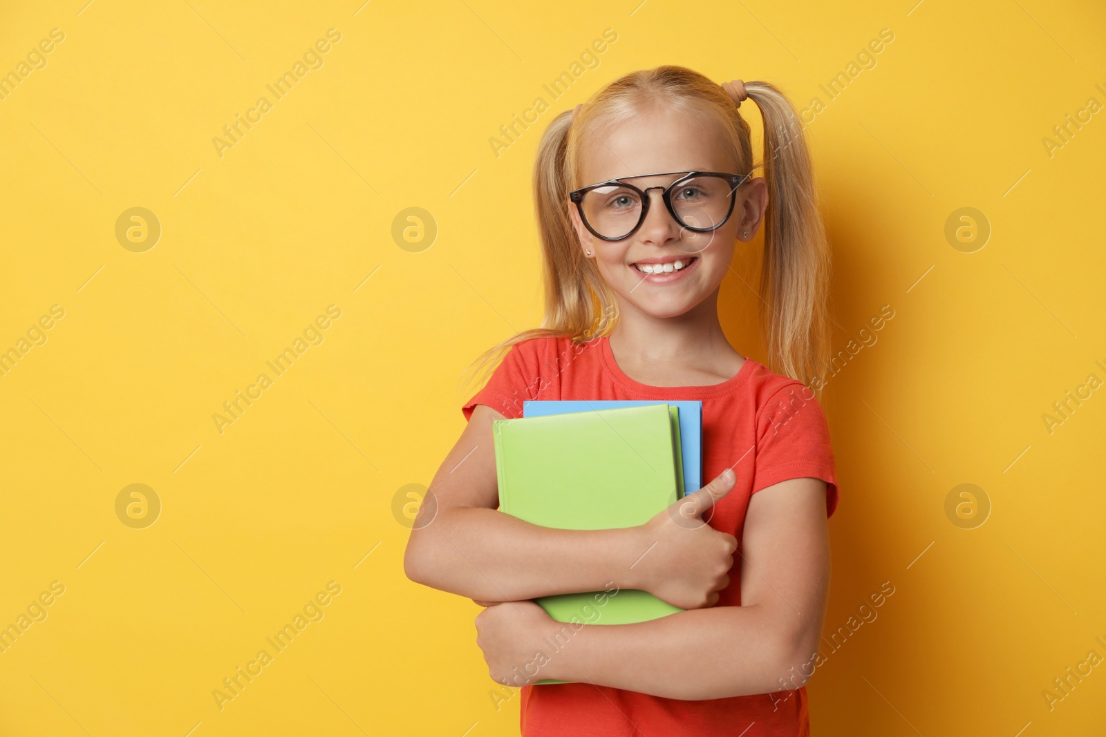 Photo of Cute little girl with glasses and books on yellow background. Reading concept