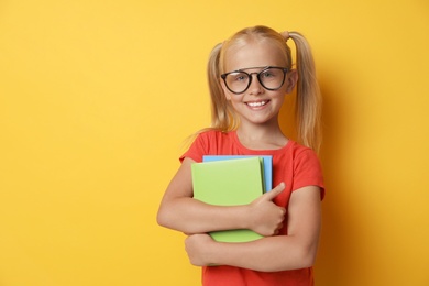 Cute little girl with glasses and books on yellow background. Reading concept