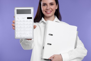 Photo of Smiling accountant with folders against purple background, focus on calculator