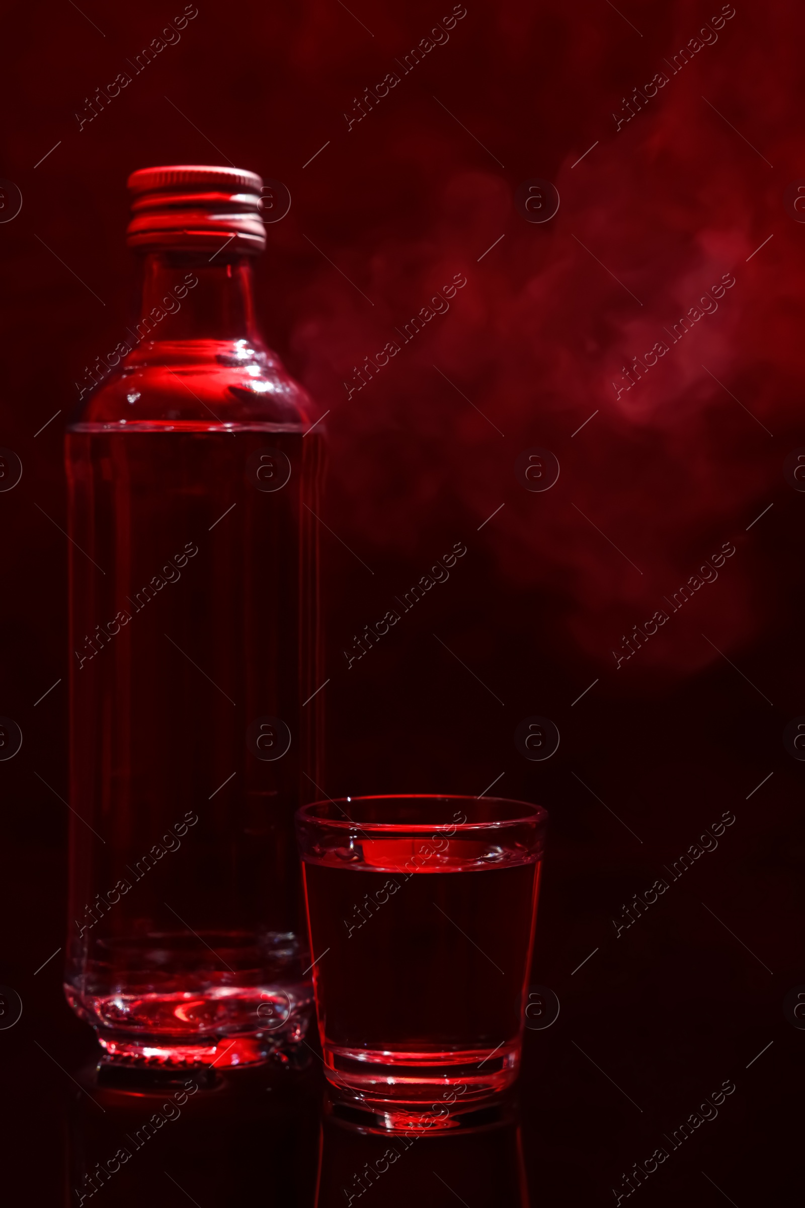 Photo of Bottle and glass with vodka on table against red background