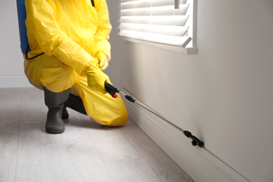 Pest control worker in protective suit spraying pesticide near window indoors, closeup