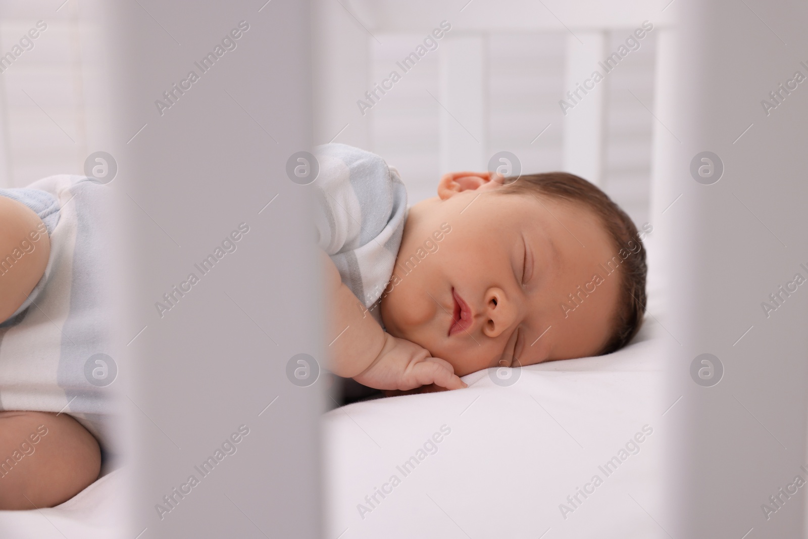 Photo of Cute newborn baby sleeping on white blanket in crib