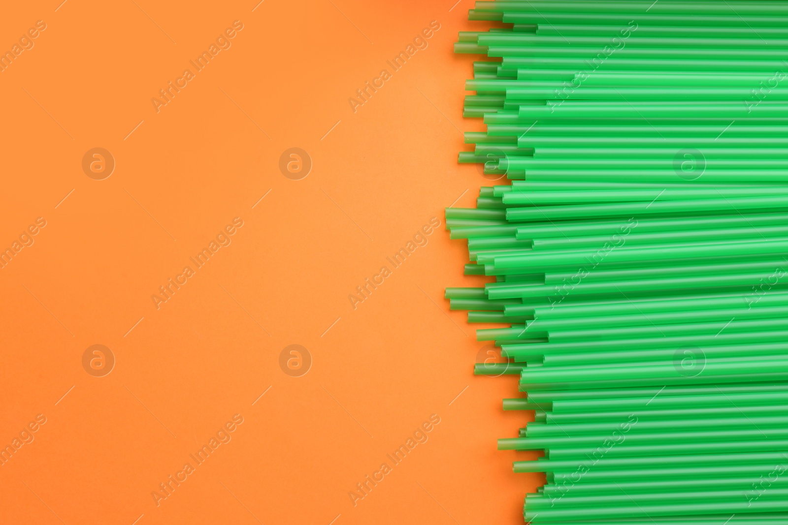 Photo of Heap of green plastic drinking straws on orange background, flat lay. Space for text