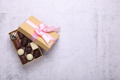 Photo of Open box with delicious chocolate candies on white table, top view. Space for text