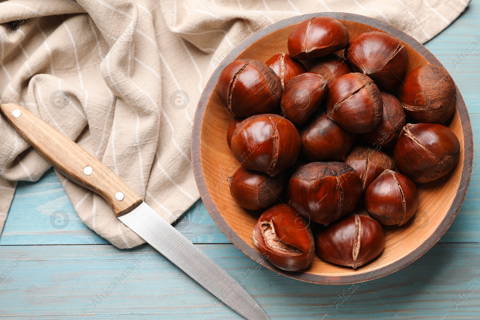 Photo of Fresh edible sweet chestnuts and knife on light blue wooden table, flat lay